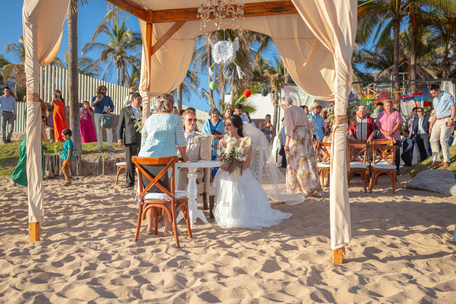 Beach wedding ceremony with bride and groom under canopy.